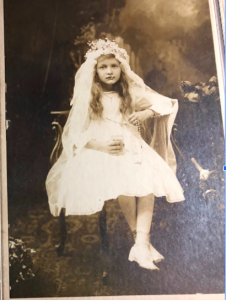 A girl in First Communion dress holding a cup and rosary
