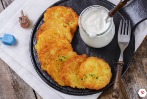 A picture of latkes and a pot of sour cream on a black tray.